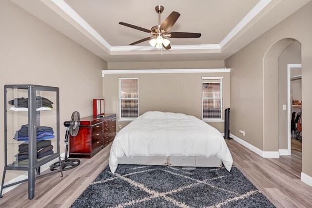 bedroom with multiple windows, a raised ceiling, arched walkways, and light wood finished floors