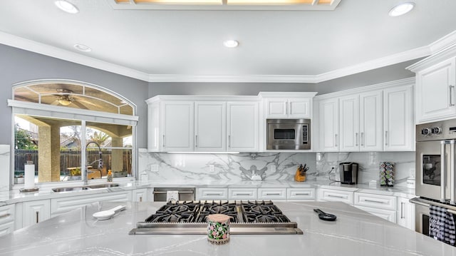 kitchen with white cabinets, a sink, stainless steel appliances, decorative backsplash, and light stone counters