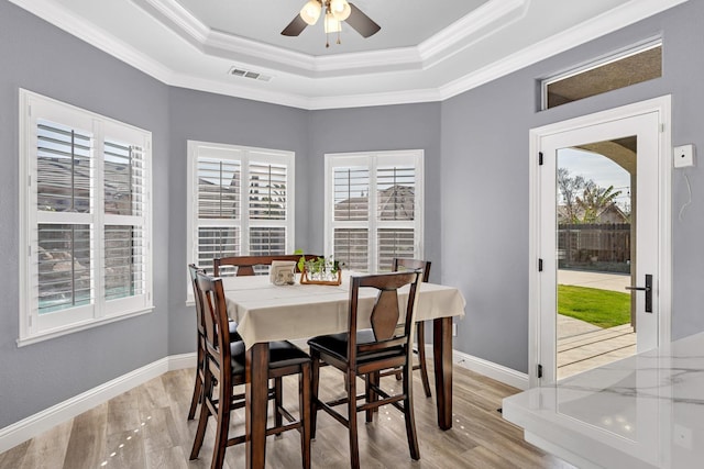dining space with light wood-style floors, a tray ceiling, ornamental molding, and visible vents