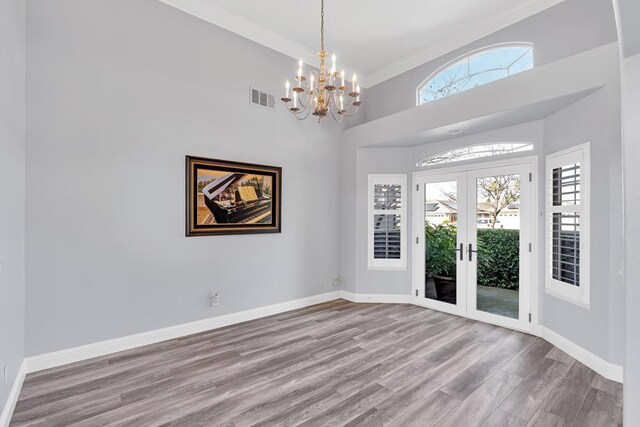 unfurnished room featuring a towering ceiling, visible vents, wood finished floors, baseboards, and a notable chandelier