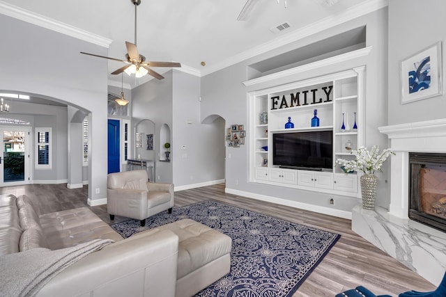 living room with crown molding, arched walkways, wood finished floors, and ceiling fan with notable chandelier