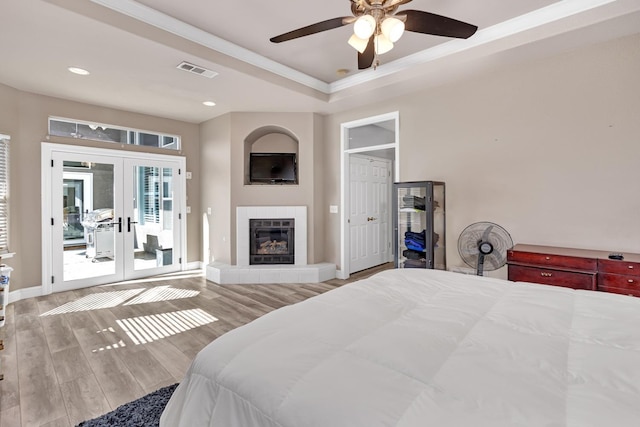 bedroom featuring a tray ceiling, visible vents, access to exterior, wood finished floors, and french doors