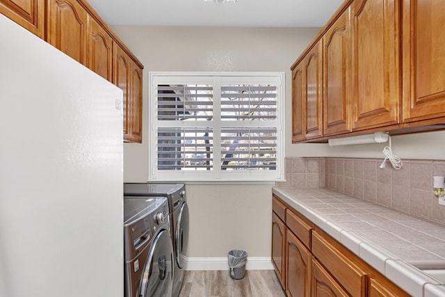 washroom with light wood-style floors, separate washer and dryer, baseboards, and cabinet space