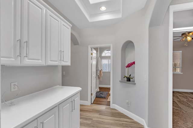 hall with recessed lighting, light wood-style floors, baseboards, and a raised ceiling