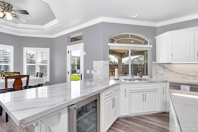 kitchen with a sink, a peninsula, wine cooler, backsplash, and light wood-style flooring