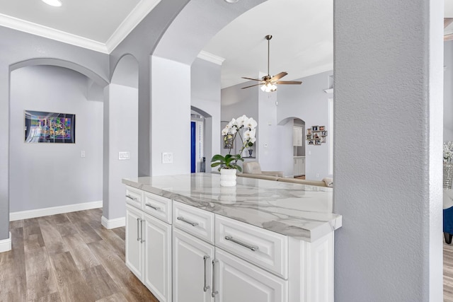 kitchen with white cabinets, a ceiling fan, light wood-style floors, crown molding, and light stone countertops