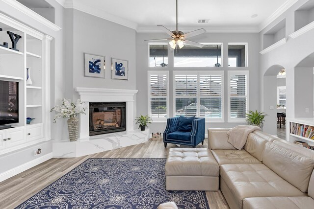 living room with arched walkways, a ceiling fan, visible vents, wood finished floors, and a high end fireplace