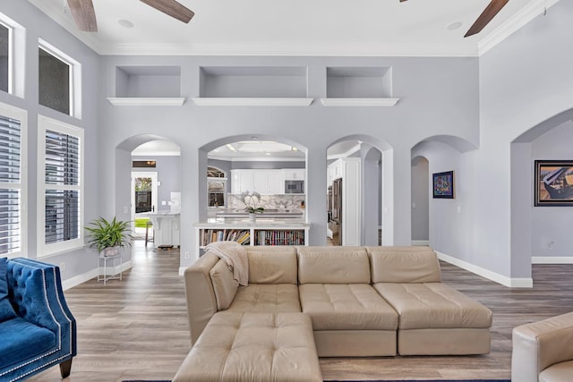 living room featuring baseboards, a ceiling fan, wood finished floors, and a towering ceiling