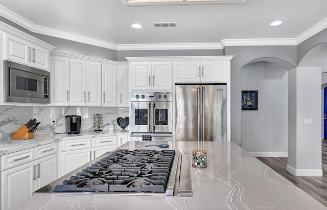 kitchen with arched walkways, white cabinetry, visible vents, light stone counters, and stainless steel appliances
