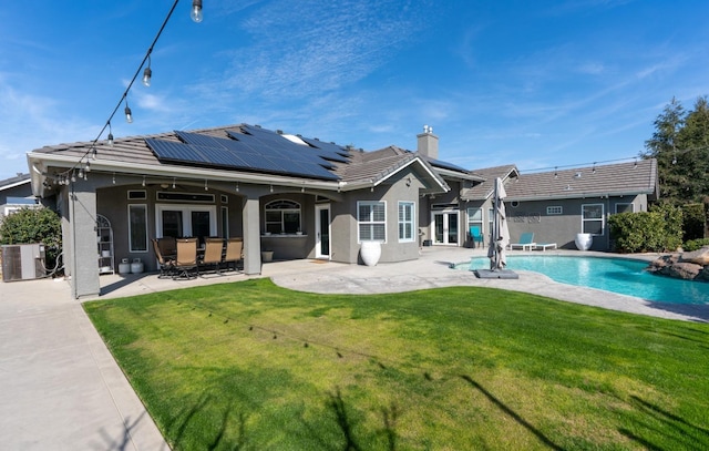 rear view of house featuring roof mounted solar panels, a ceiling fan, a lawn, a patio, and french doors