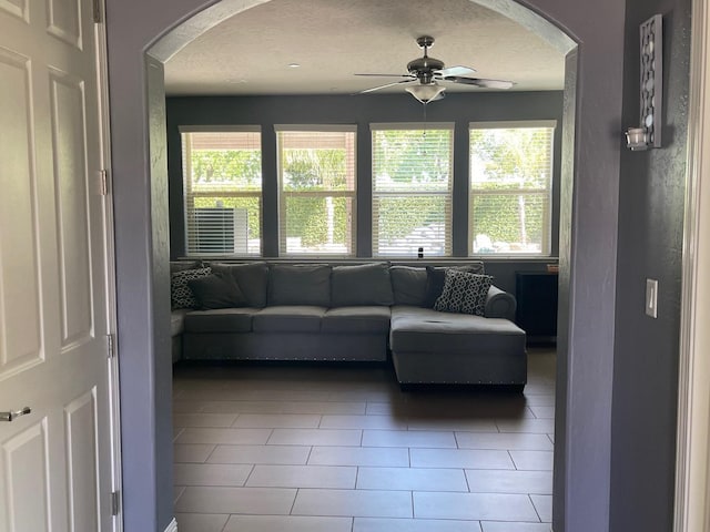 living area featuring arched walkways, a ceiling fan, tile patterned flooring, and a textured ceiling