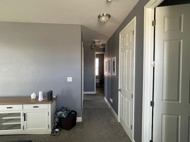 hallway with visible vents, baseboards, and dark colored carpet