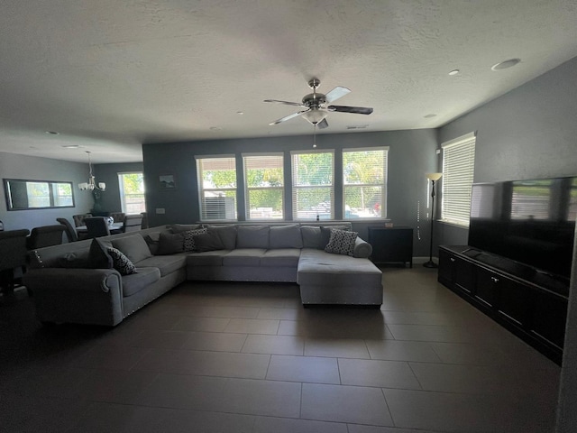 living room with a textured ceiling, ceiling fan with notable chandelier, and dark tile patterned floors