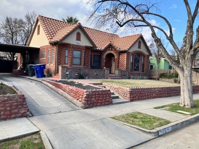 tudor-style house featuring brick siding, driveway, a tiled roof, and fence