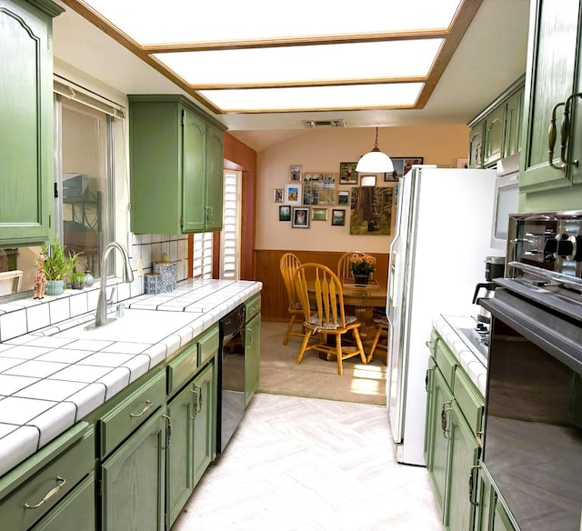 kitchen with green cabinets, tile countertops, a sink, black dishwasher, and oven