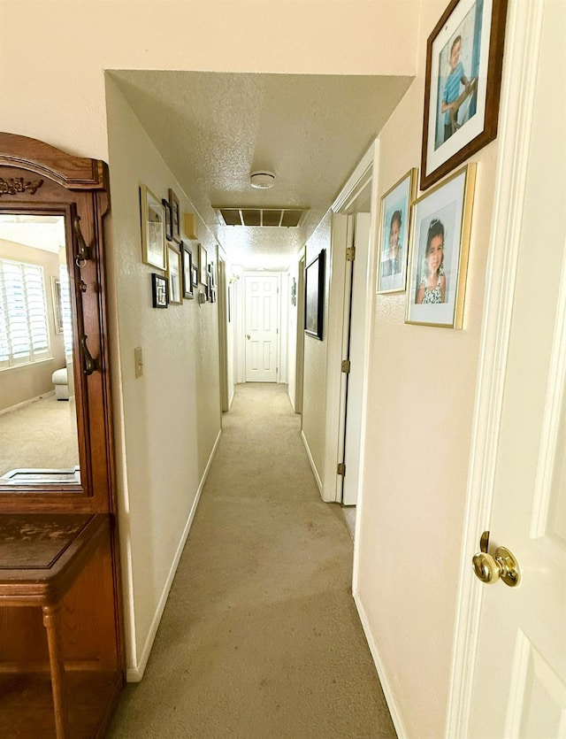 hallway with light colored carpet, baseboards, and a textured ceiling