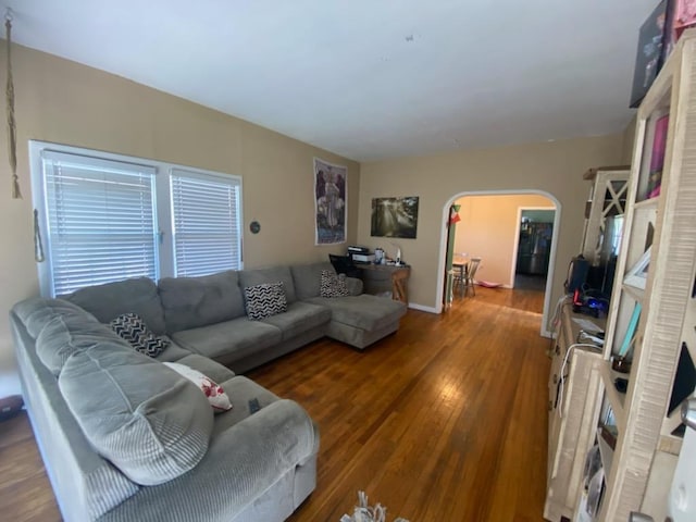 living area with arched walkways, baseboards, and wood finished floors