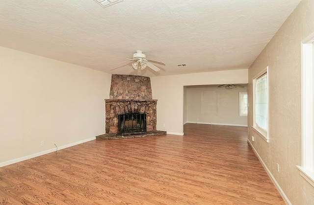 unfurnished living room featuring baseboards, a stone fireplace, light wood-type flooring, a textured ceiling, and a ceiling fan