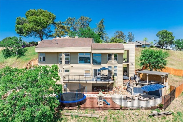back of house with a trampoline, a patio, fence, and a playground