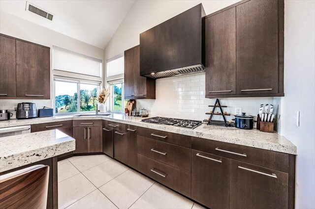 kitchen with dark brown cabinets, vaulted ceiling, visible vents, custom exhaust hood, and decorative backsplash