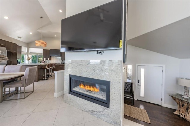 living area with a glass covered fireplace, recessed lighting, light tile patterned flooring, visible vents, and lofted ceiling