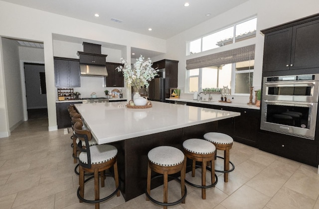 kitchen with wall chimney range hood, a breakfast bar, appliances with stainless steel finishes, light countertops, and a sink
