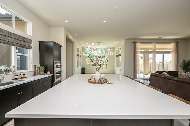 kitchen featuring a large island, a sink, open floor plan, light countertops, and double oven
