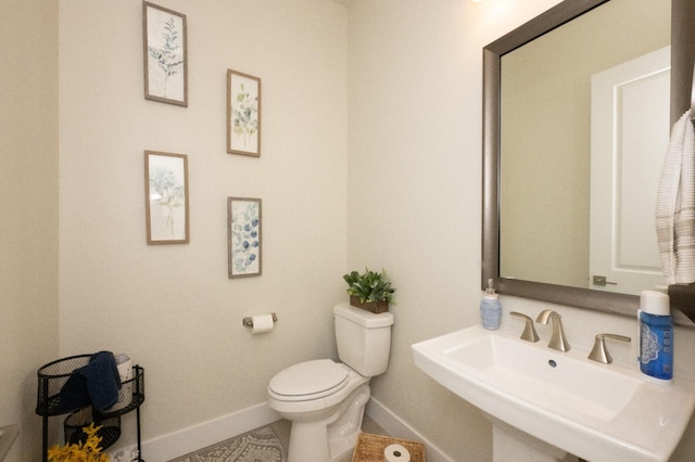 half bathroom featuring toilet, a sink, and baseboards