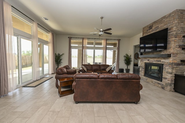 living room with visible vents, a stone fireplace, and a ceiling fan