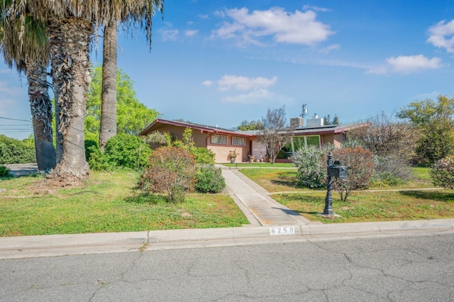 ranch-style house featuring concrete driveway, stucco siding, a front lawn, and roof mounted solar panels