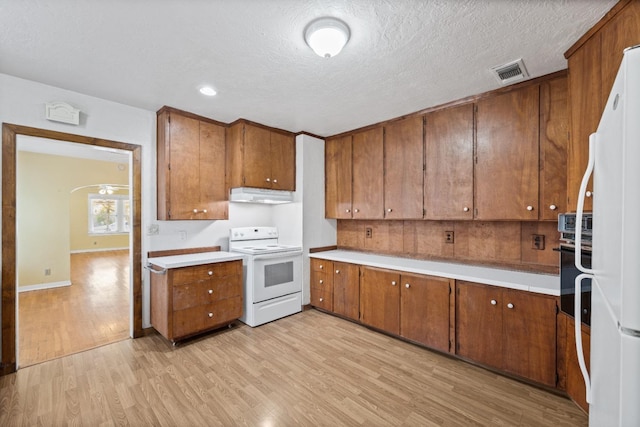 811 E Cambridge Ave, Fresno, CA 93704 - kitchen featuring white appliances, under cabinet range hood, brown cabinetry, light wood finished floors, and a textured ceiling