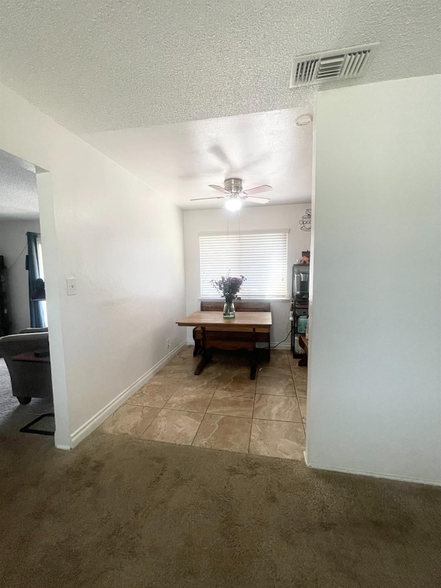 hall with visible vents, a textured ceiling, light tile patterned floors, and light colored carpet