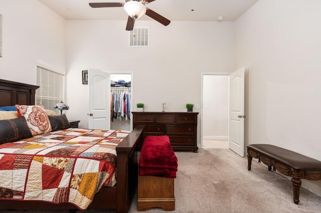 bedroom with ceiling fan, light colored carpet, a towering ceiling, visible vents, and a walk in closet