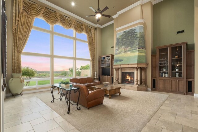 living area featuring a ceiling fan, visible vents, ornamental molding, a warm lit fireplace, and a high ceiling