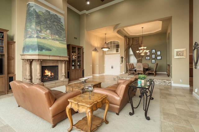 living room with a towering ceiling, a fireplace, baseboards, an inviting chandelier, and ornamental molding