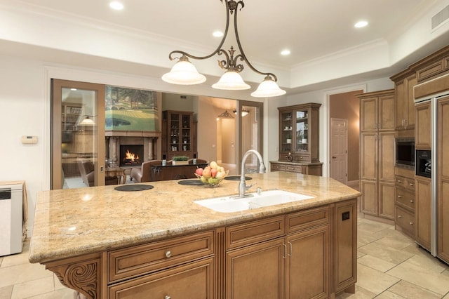 kitchen featuring built in appliances, a kitchen island with sink, glass insert cabinets, a warm lit fireplace, and a sink