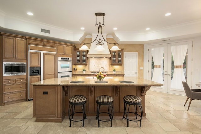 kitchen featuring built in appliances, brown cabinetry, a large island, decorative backsplash, and visible vents