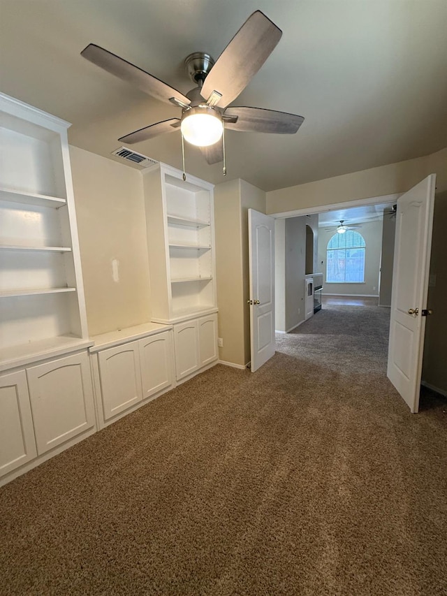empty room featuring dark carpet, built in features, baseboards, and ceiling fan