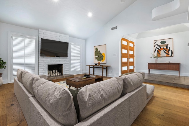living area with hardwood / wood-style flooring, visible vents, baseboards, arched walkways, and a fireplace