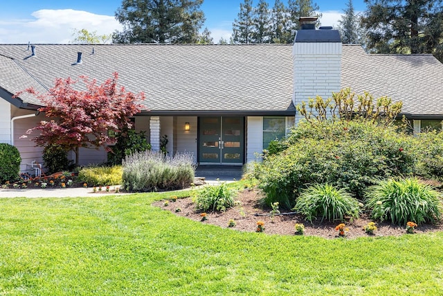 view of front of property with roof with shingles, a chimney, and a front lawn