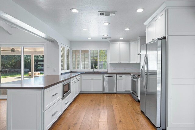 kitchen featuring white cabinets, a sink, appliances with stainless steel finishes, light wood-style floors, and a peninsula