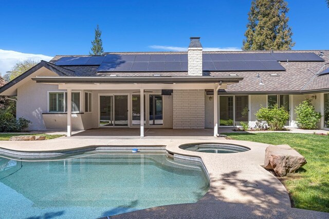 rear view of property featuring a patio area, an outdoor pool, an in ground hot tub, a chimney, and roof mounted solar panels