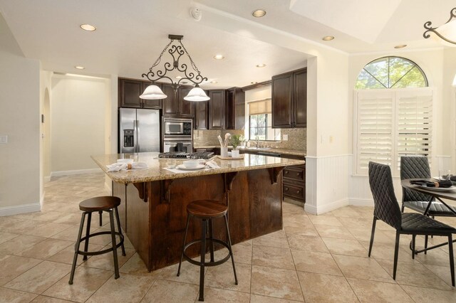 10001 N Pheasant Run Dr, Fresno, CA 93730 - kitchen featuring stainless steel appliances, dark brown cabinetry, light stone counters, a kitchen bar, and backsplash