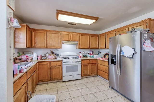 kitchen featuring brown cabinets, stainless steel fridge with ice dispenser, white gas range oven, light countertops, and under cabinet range hood