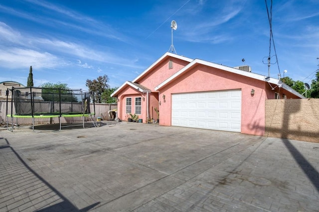 single story home with fence, stucco siding, an attached garage, concrete driveway, and a trampoline