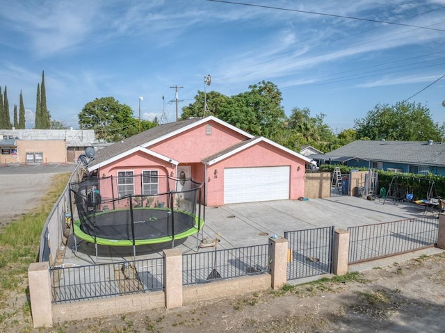 view of front facade featuring concrete driveway, stucco siding, a trampoline, fence private yard, and a garage