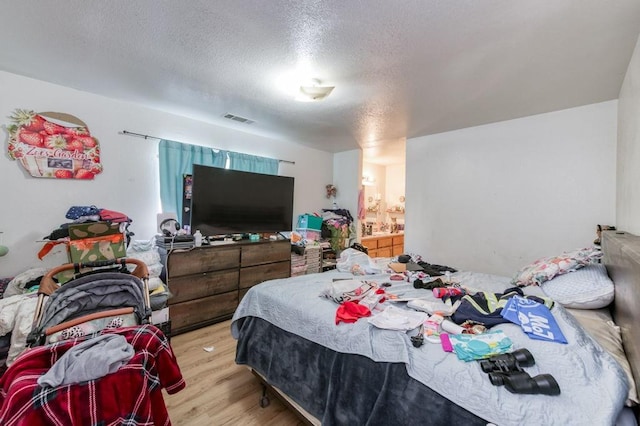 bedroom featuring a textured ceiling, light wood-type flooring, visible vents, and connected bathroom