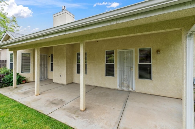 back of property featuring a chimney, a patio, and stucco siding