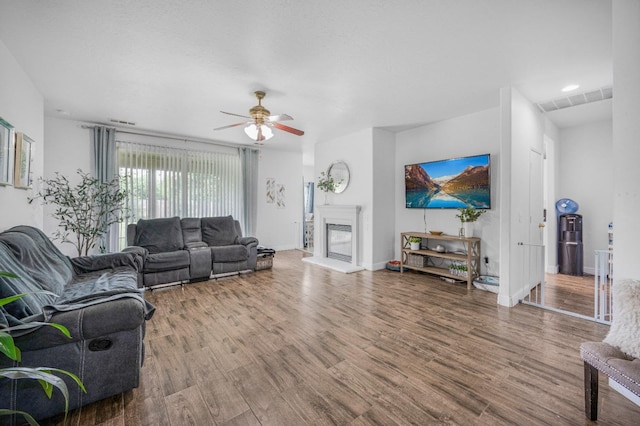 living room featuring baseboards, a ceiling fan, wood finished floors, and a fireplace with raised hearth