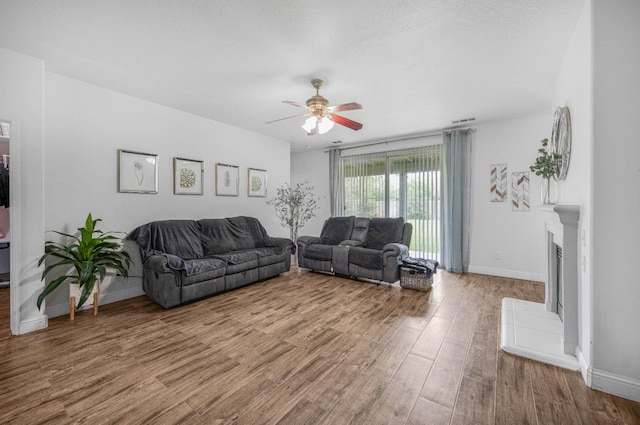 living room featuring a fireplace with raised hearth, wood finished floors, visible vents, a ceiling fan, and baseboards